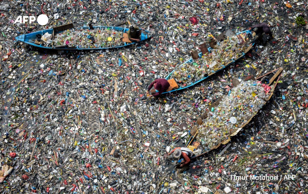 People on boats collect recyclable plastics in a river