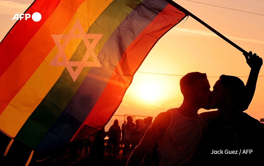 Two participants kiss while holding a pride rainbow flag